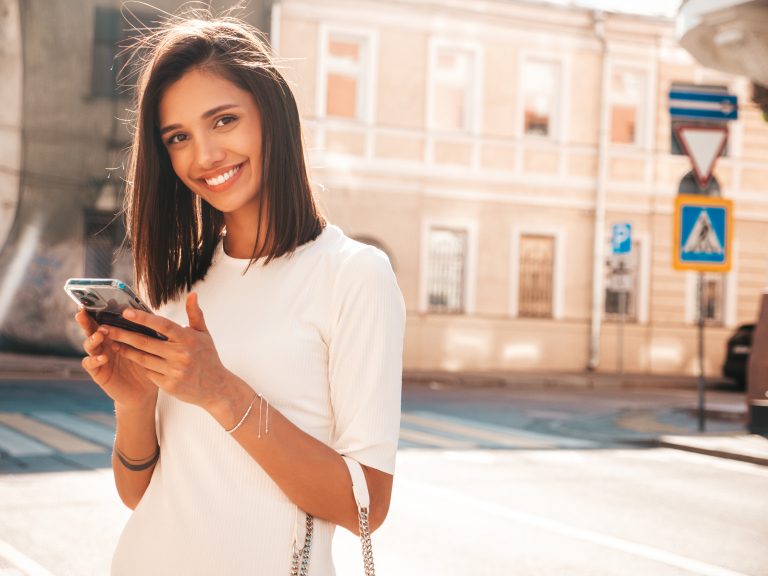 Smiling woman using smartphone outdoors, representing seamless customer engagement with Mocean’s SMS API